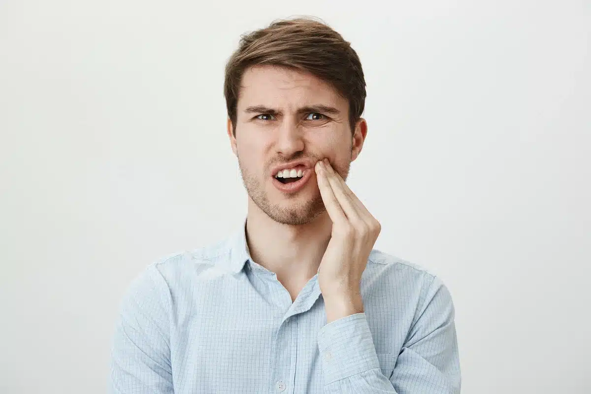man touching his cheek because of heavy tooth nerve pain